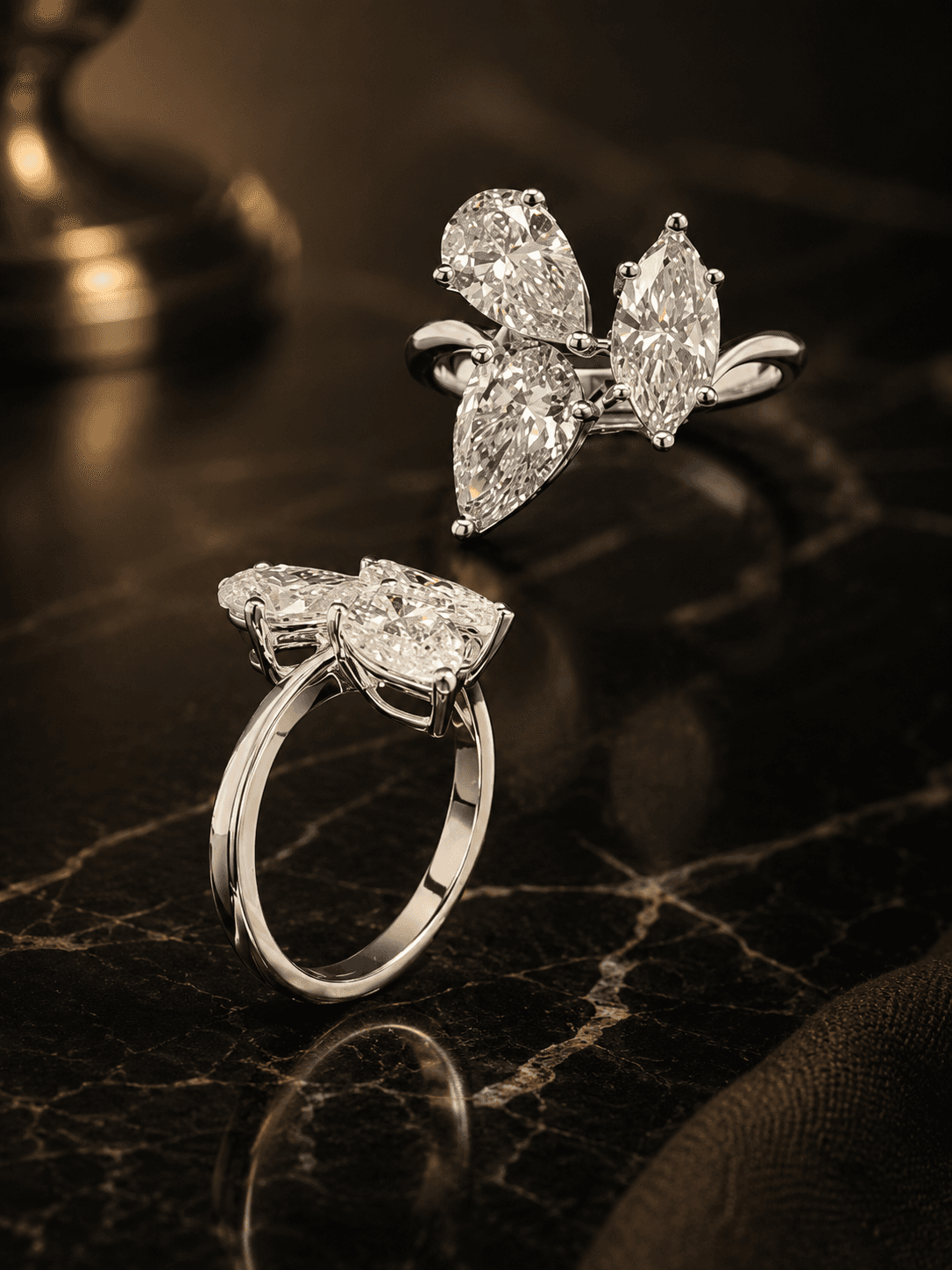 Two sculptural cluster rings pairing pear and marquise lab-grown diamonds in white gold, on black marble.