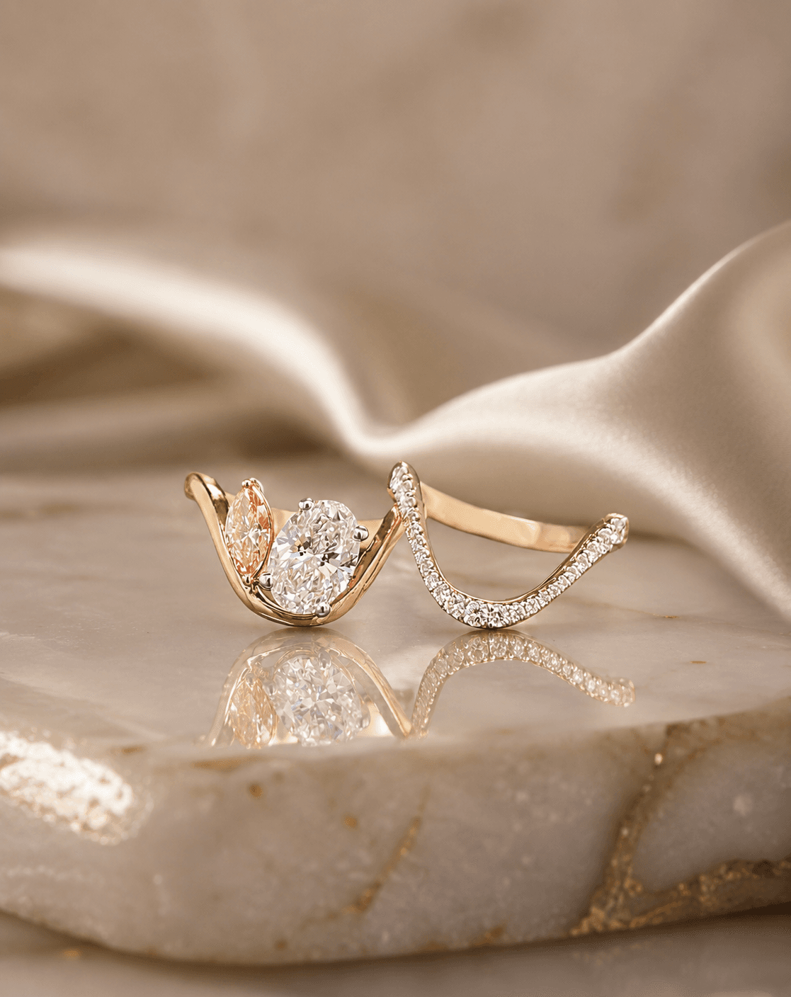 Toi-et-moi ring pairing a white oval and a pink marquise lab-grown diamond in yellow gold, with a curved pavé contour band, on ivory stone.